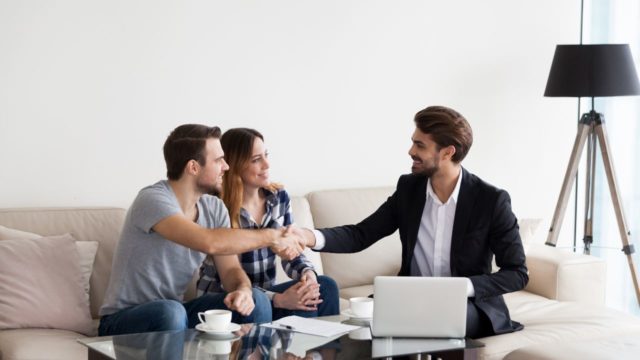 property-manager-sitting-on-couch-with-a-couple-of-tenants-shaking-their-hands