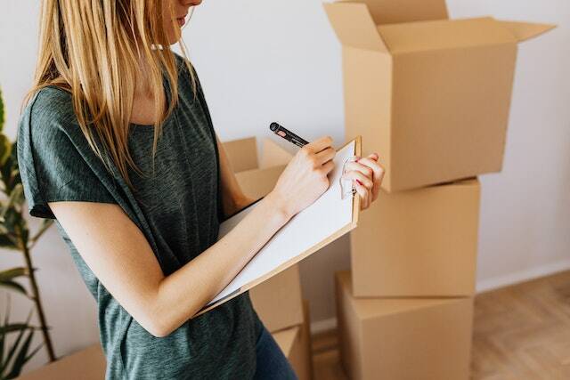 person taking notes on clipboard with cardboard boxes in the background